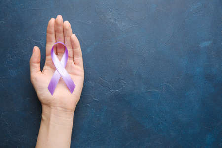 Female hand with lilac ribbon on color background. Cancer awareness conceptの写真素材