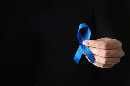 Female hand with blue ribbon on dark background. Cancer awareness conceptの写真素材