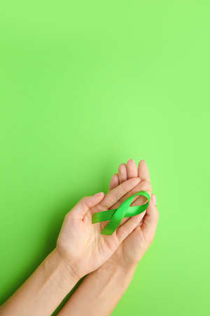 Female hands with green ribbon on color background. Cancer awareness conceptの写真素材
