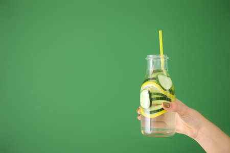 Female hand with bottle of healthy infused water on color backgroundの写真素材