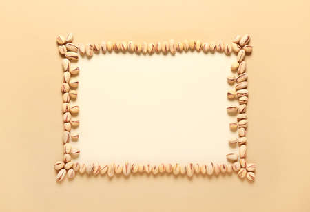 Frame made of tasty pistachio nuts on color background