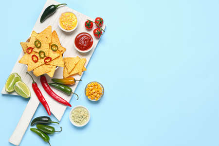 Board with tasty nachos, sauces and chili pepper on color backgroundの写真素材