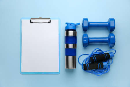 Dumbbells with clipboard, jumping rope and bottle of water on color backgroundの写真素材
