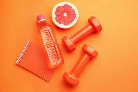 Dumbbells with notebook, grapefruit and bottle of water on color backgroundの写真素材
