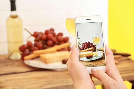 Female food photographer with mobile phone taking picture of cheese and wineの写真素材