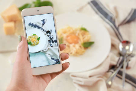 Female food photographer with mobile phone taking picture of pastaの写真素材