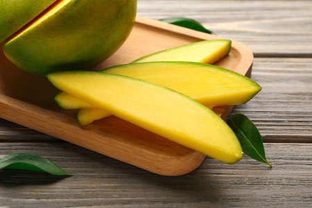 Plate with cut mango fruit on wooden background
