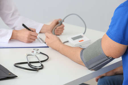 Doctor measuring blood pressure of young man in clinicの写真素材