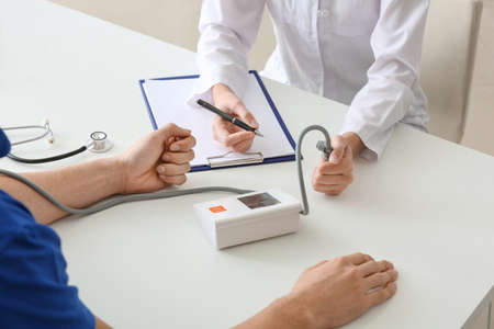 Doctor measuring blood pressure of young man in clinic