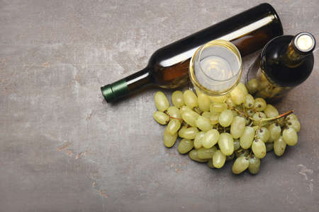 Bottles and glass of wine with grapes on gray backgroundの写真素材