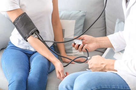 Doctor measuring blood pressure of young woman at homeの写真素材