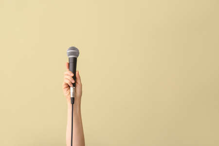 Female hand with microphone on color background