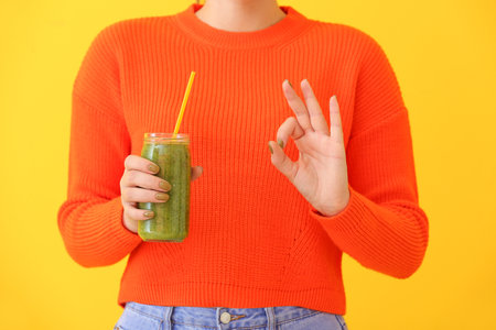 Woman with jar of healthy smoothie showing OK on color backgroundの写真素材