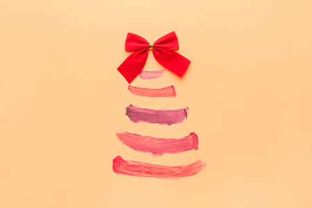 Beautiful Christmas tree made of lipstick strokes and bow on color backgroundの写真素材