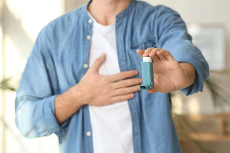 Sick man with asthma inhaler at home, closeup
