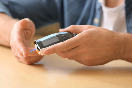Diabetic man checking blood sugar level at table, closeup
