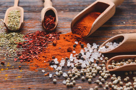 Scoops with different spices on wooden background