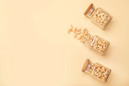 Jars with tasty cashew nuts on color background