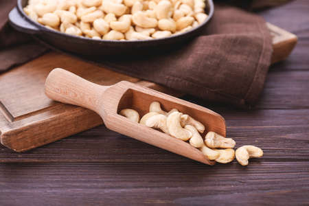 Scoop and frying pan with tasty cashew nuts on wooden backgroundの写真素材