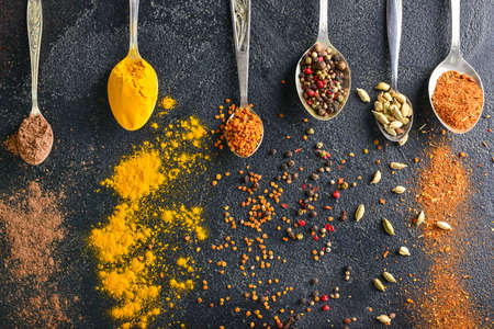 Spoons with different spices on dark background
