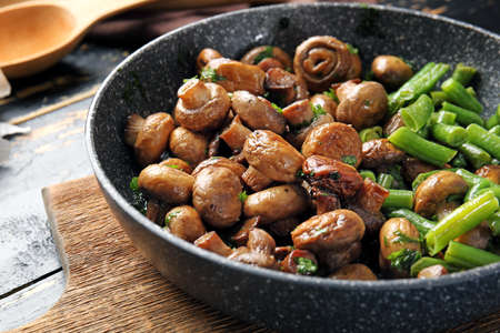 Frying pan with tasty cooked mushrooms and green beans on tableの写真素材