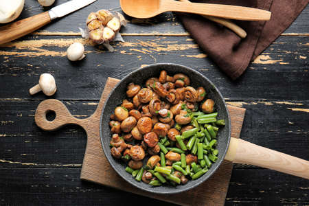 Frying pan with tasty cooked mushrooms and green beans on tableの写真素材