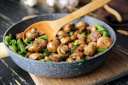 Frying pan with tasty cooked mushrooms and green beans on tableの写真素材