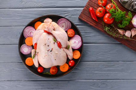 Frying pan with raw chicken and vegetables on wooden backgroundの写真素材