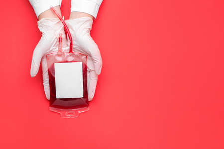 Hands of doctor with blood pack for transfusion on color backgroundの写真素材