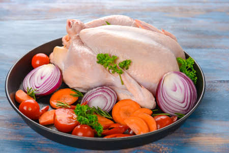 Frying pan with raw chicken and vegetables on wooden backgroundの写真素材