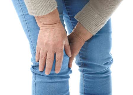 Senior woman suffering from pain in knee on white background, closeup