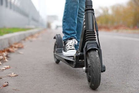 Teenage boy riding kick scooter outdoors, closeup