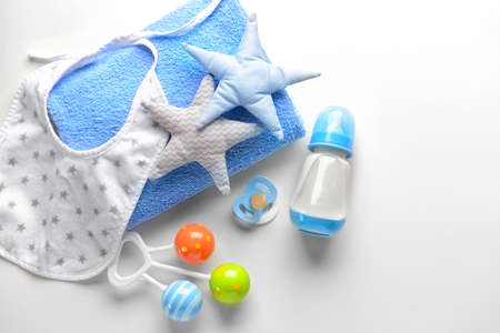 Bottle of milk for baby with toys, towel, bib and pacifier on white background