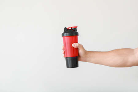 Male hand with protein shake on light backgroundの写真素材