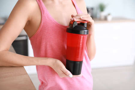 Sporty young woman with protein shake at home, closeup
