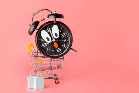 Funny alarm clock and cart on color background. Time for shoppingの写真素材