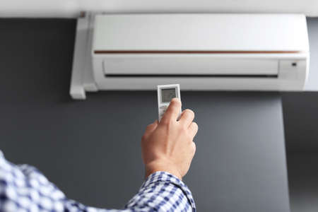 Young man switching on air conditioner at home closeup