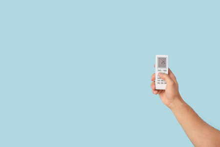Male hand with air conditioner remote control on color background