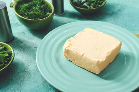 Plate with fresh butter and herbs on table
