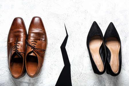 Crack between two pairs of shoes on light background. Concept of divorce