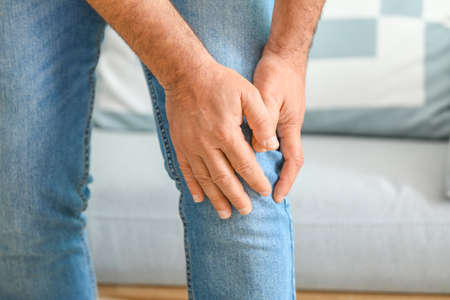 Mature man suffering from pain in knee at home, closeup