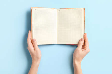 Female hands with blank notebook on color background