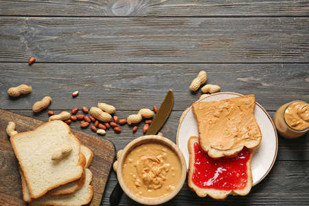 Tasty peanut butter in bowl and fresh bread with jam on wooden tableの写真素材