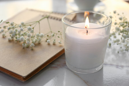 Burning candle, notebook and flowers on tableの写真素材