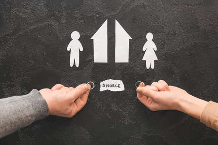 Male and female hands with wedding rings, cut figures of house and couple on dark background....