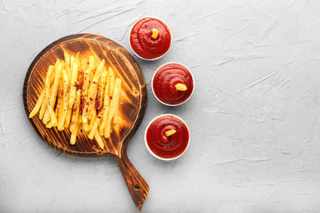 Tasty french fries and tomato sauce on gray background