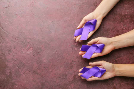 Female hands with purple ribbons as symbol of World Cancer Day on color background