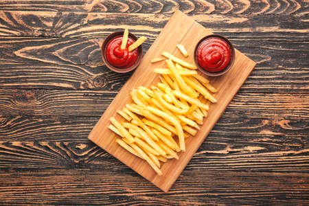 Tasty french fries and tomato sauce on wooden background