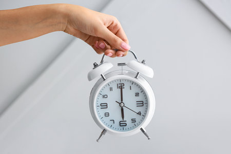 Female hand with alarm clock on gray background