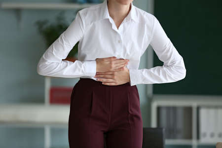 Young businesswoman suffering from abdominal pain in officeの写真素材